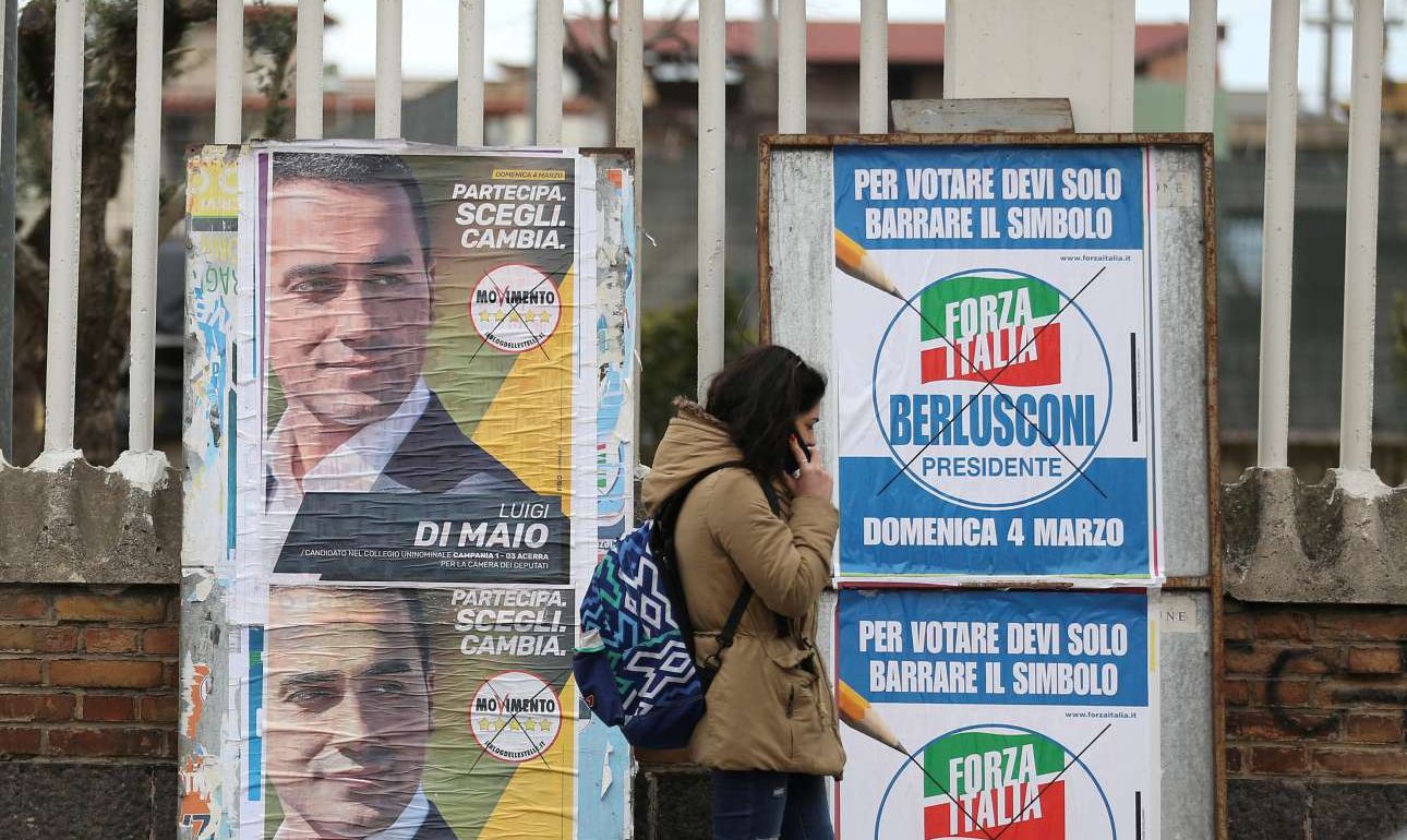 Μία κοπέλα μιλάει στο τηλέφωνο μπροστά από τις προεκλογικές αφίσες των δύο πρωταγωνιστών. Του Κινήματος 5 αστέρων με επικεφαλής τον Ντι Μάιο και του Forza Italia,το κόμμα του «Καβαλιέρε» (REUTERS/ Alessandro Bianchi/ File Photo)